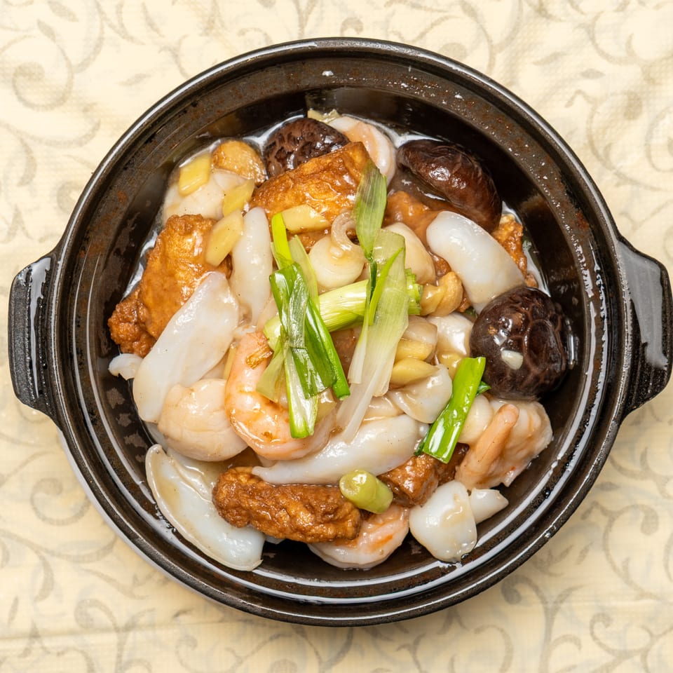 A clay pot filled with stir-fried shrimp, squid, mushrooms, tofu, and green onions.