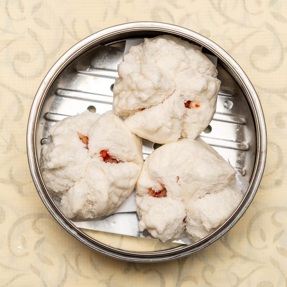Three fluffy white char siu bao (steamed pork buns) in a metal dim sum steamer basket.